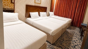 Habitación de hotel con tres camas, alfombra estampada, cabecera de madera y cortina roja.