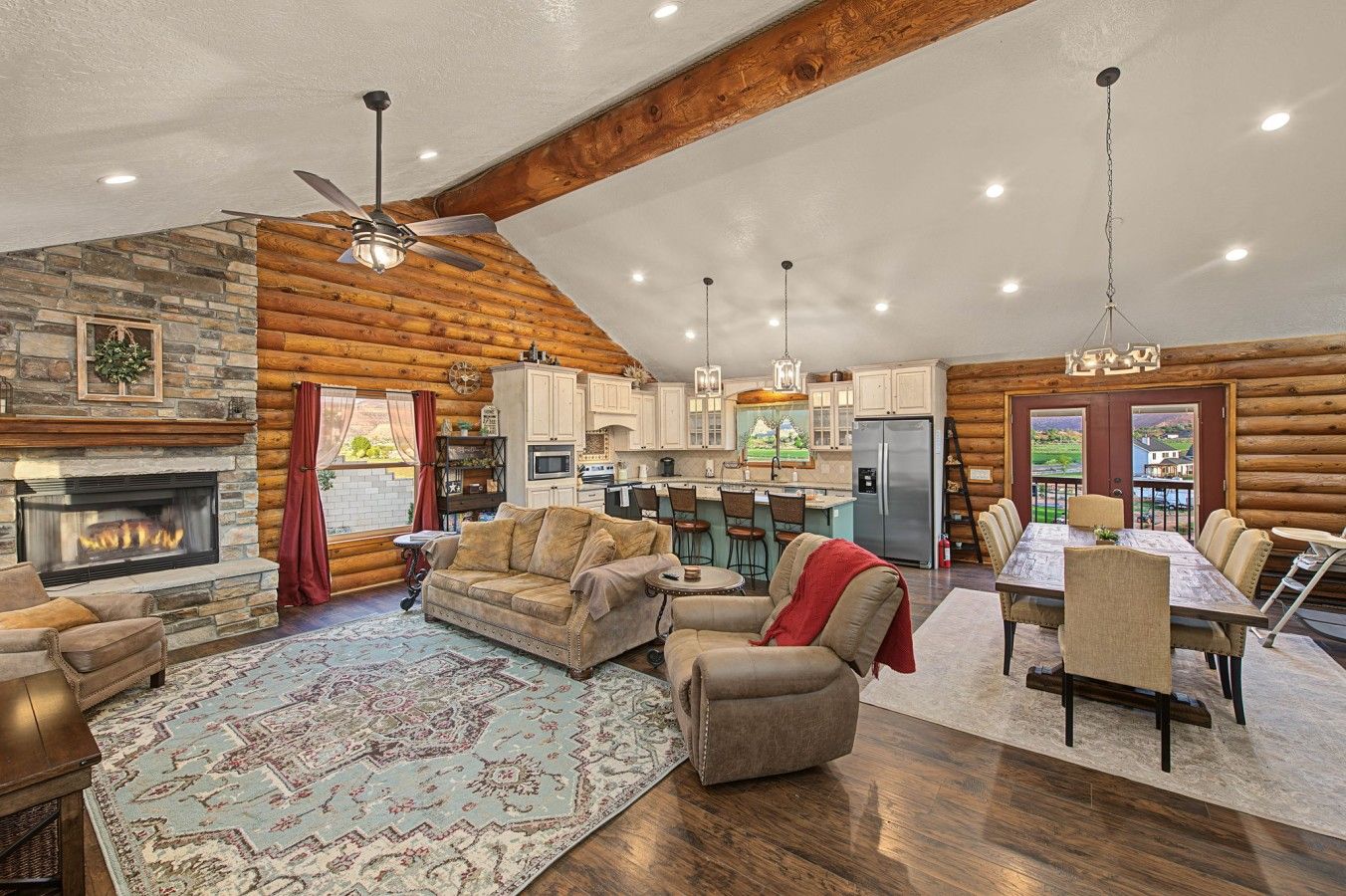 A log cabin interior with a fireplace, dining area, kitchen, and a ceiling fan.
