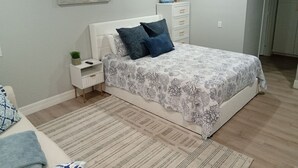Quarto com cama, mesa de cabeceira, cômoda e um quadro na parede.