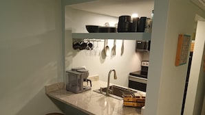 Cozinha compacta com bancada, pia e fogão. Há três banquetas e uma cafeteira.
