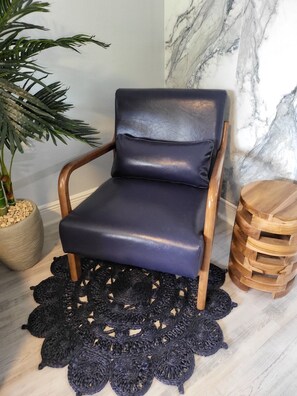 Ein Sessel mit dunkler Polsterung, ein Blumentopf, eine Marmorwand und ein Holztischchen.