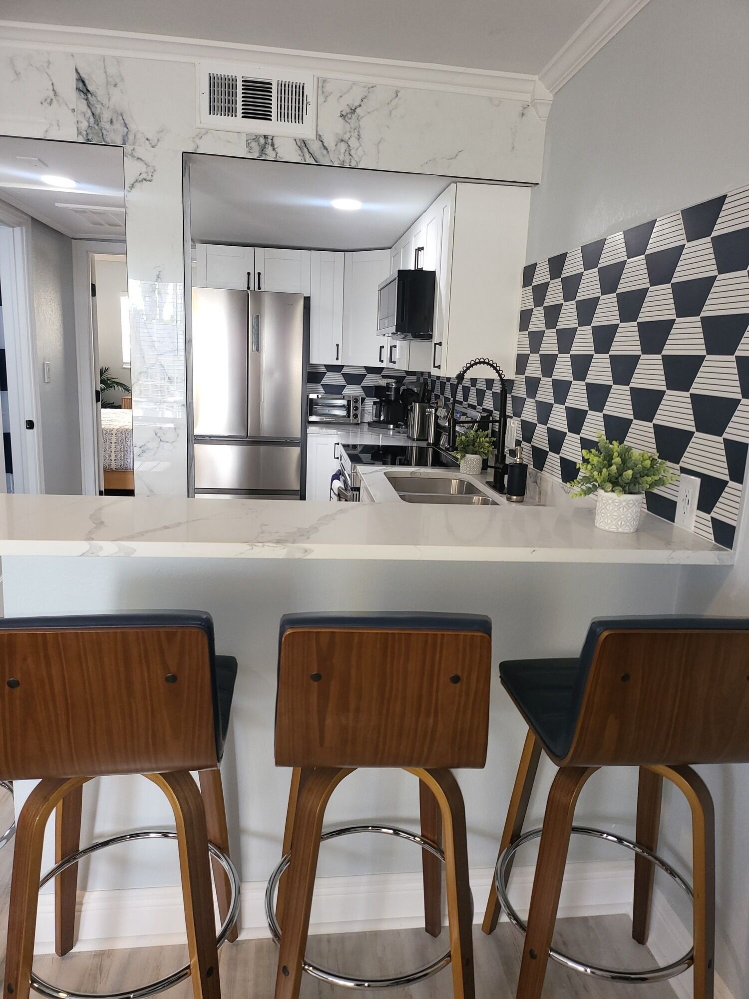 A modern kitchen with a marble backsplash, stainless steel appliances, and a geometric-patterned wall.