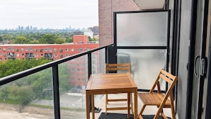 Ein Balkon mit Tisch und Stühlen, Blick auf die Stadtlandschaft, und ein Gebäude mit Glastür.