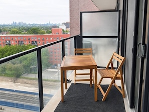 Un balcone con tavolo e sedie, vista sulla città e un edificio con una porta in vetro.