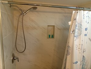 A shower area with a handheld showerhead, a glass-enclosed medicine cabinet, and a shower curtain with a nautical pattern. - Unit 111 - Beach Getaway (2nd Floor) (Treasure Island)
