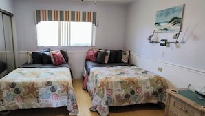 Ein Schlafzimmer mit zwei Betten, einem Schminktisch, einem Fernseher und einem Fenster mit Vorhängen.