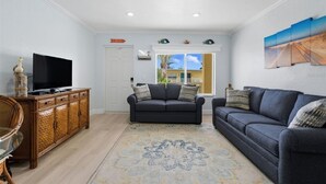 Uma sala de estar com televisão sobre um armário de madeira, um sofá escuro e um tapete estampado.