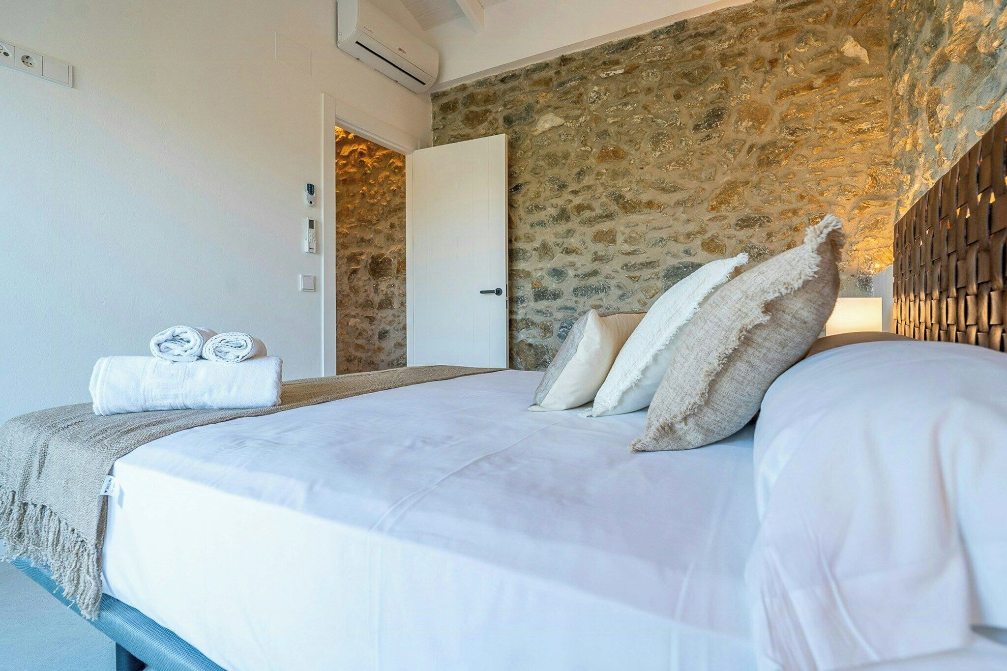 A bedroom with a stone wall, a bed with white bedding, and a door leading to another room.