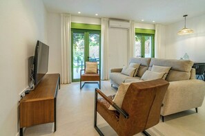 A modern living room with a sofa, armchair, TV, and a dining area with chairs. - Beautiful House in Álora with Pool and Views (Álora)