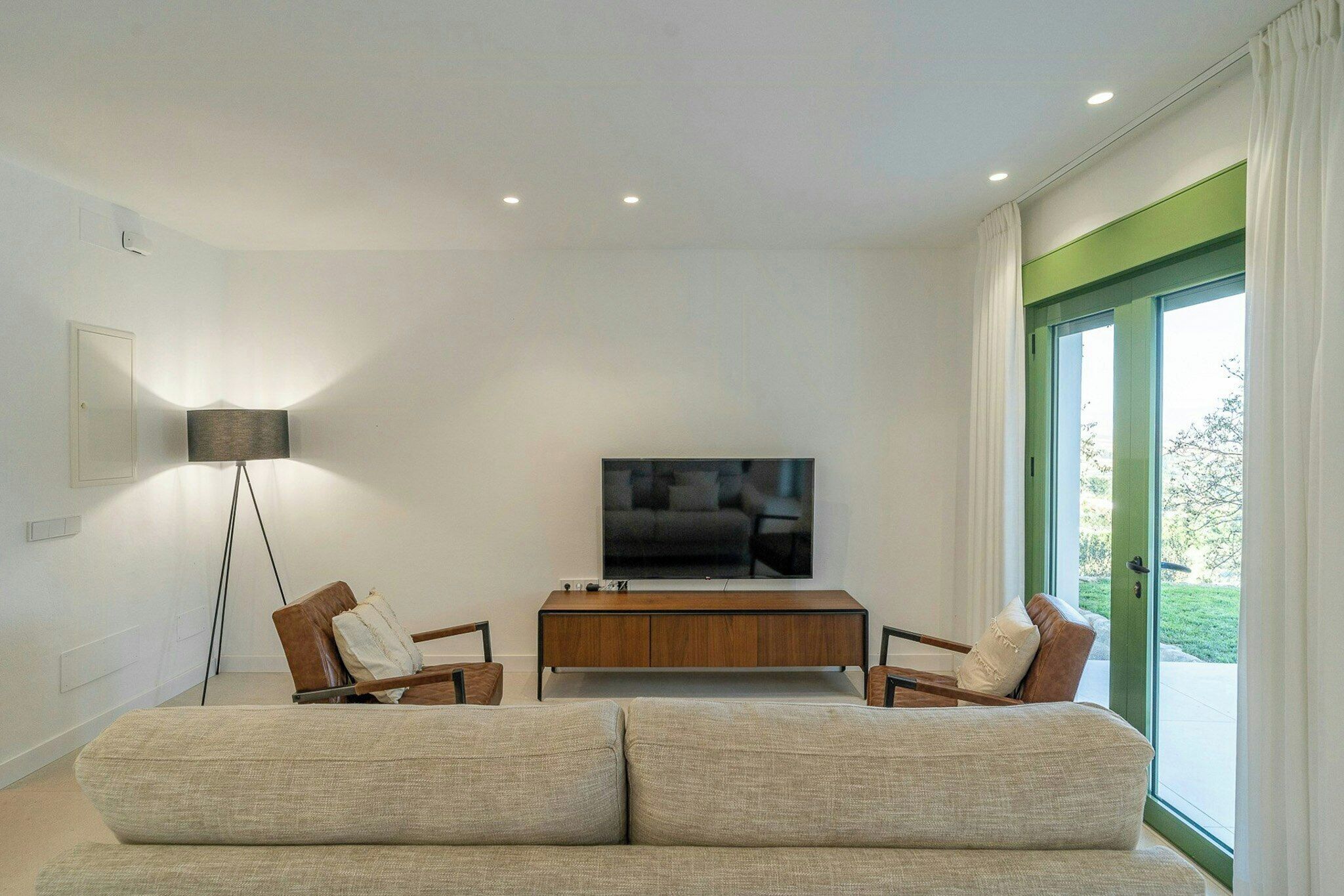 A modern living room with a sofa, two armchairs, a coffee table, a flat-screen TV, and a floor lamp.