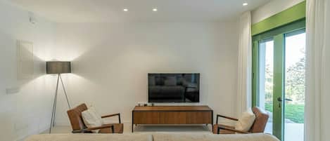 A modern living room with a sofa, two armchairs, a coffee table, a flat-screen TV, and a floor lamp.