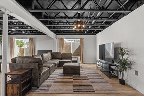 A modern living room with a sectional sofa, a flat-screen TV, and a large window with curtains.