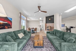 A modern living room with green sofas, a wooden coffee table, and a dining area with chairs. - 35-Acre Retreat w/ Private Canyon & Hot Tub (Florence)