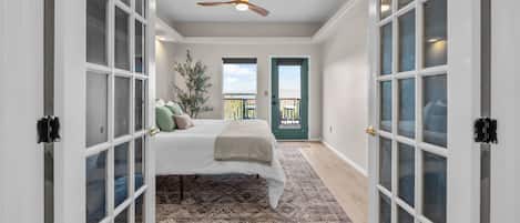 A bedroom with a bed, a ceiling fan, and a view through a door.