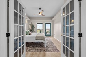 A bedroom with a bed, a ceiling fan, and a view through a door.