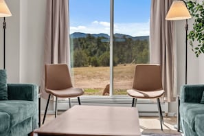 Una habitación con dos sillas mirando a un ventanal grande, una mesa y dos lámparas.