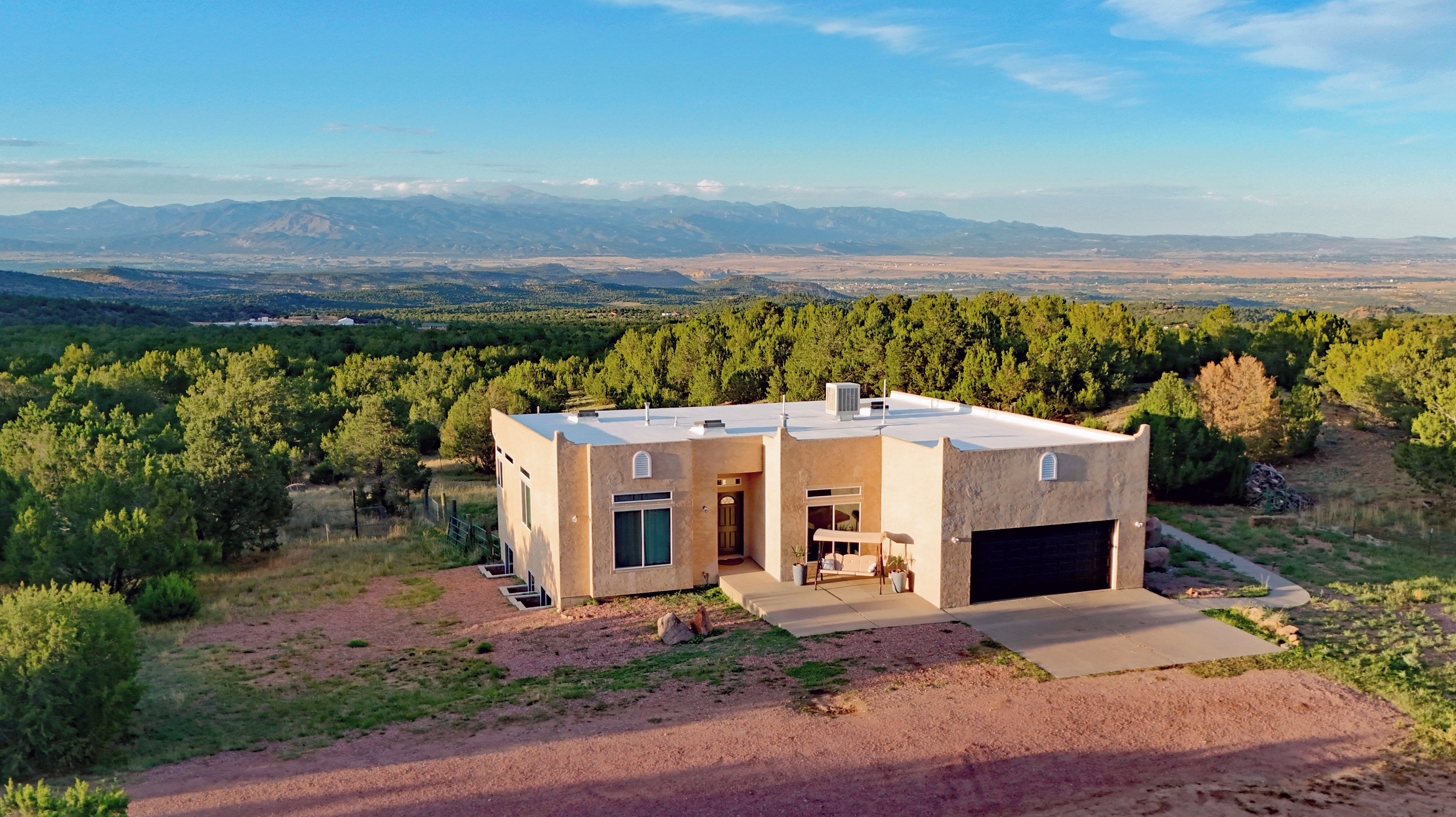 Una casa moderna de dos pisos con garaje, rodeada de un paisaje natural y montañas al fondo.