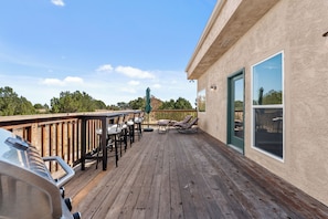 A wooden deck with outdoor furniture, a grill, and a view of the surrounding landscape.