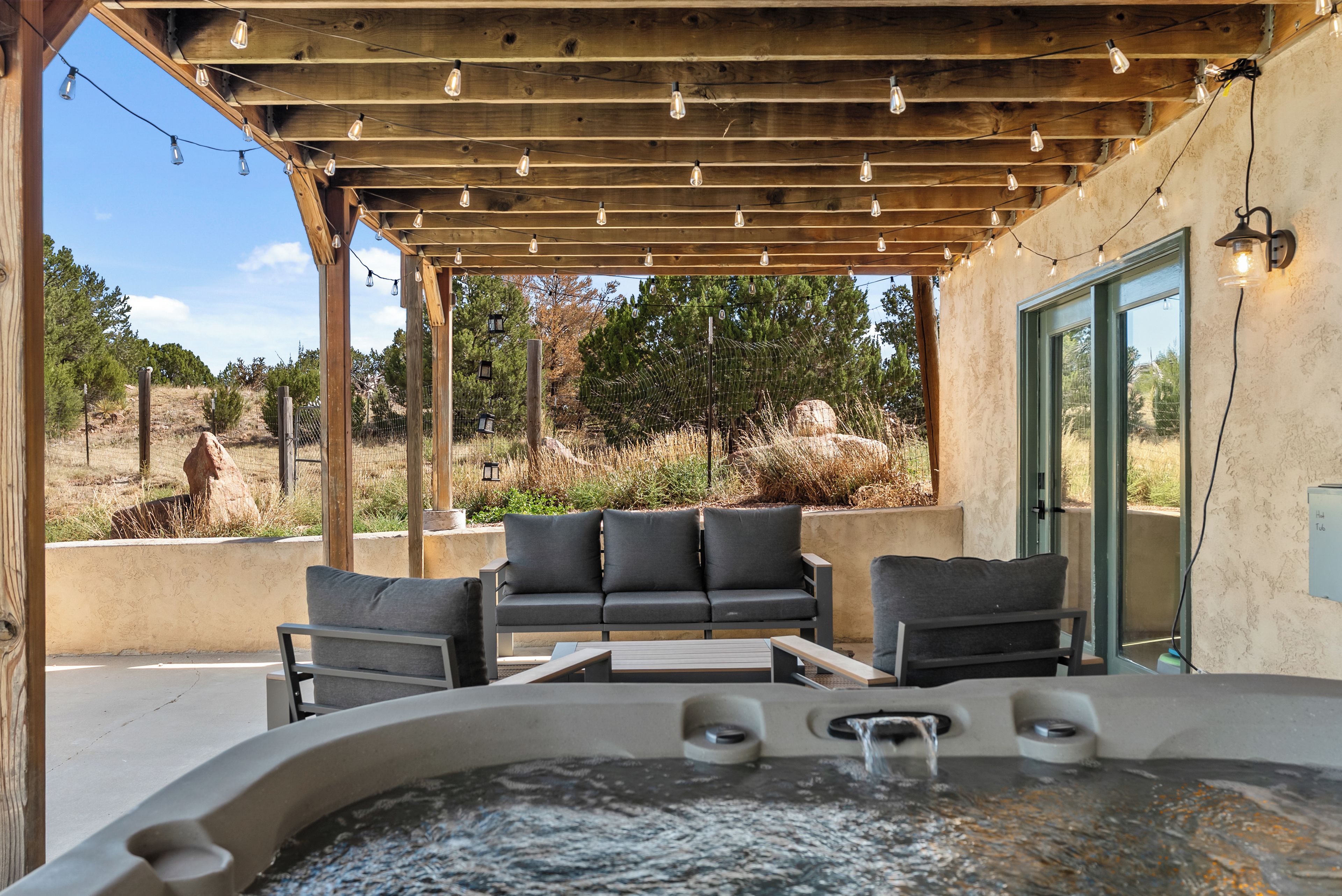 An outdoor patio with a hot tub, wooden pergola, and seating area.