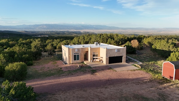 A modern two-story house with a garage, surrounded by a natural landscape and distant mountains.