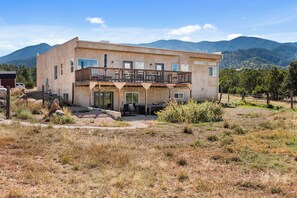 A two-story building with a balcony, surrounded by a dry grassy landscape and mountains in the background.