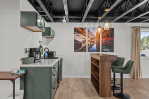 A modern kitchen with a coffee machine, a sink, and a bar area with stools. There are two large paintings on the wall. - 35-Acre Retreat w/ Private Canyon & Hot Tub (Florence)