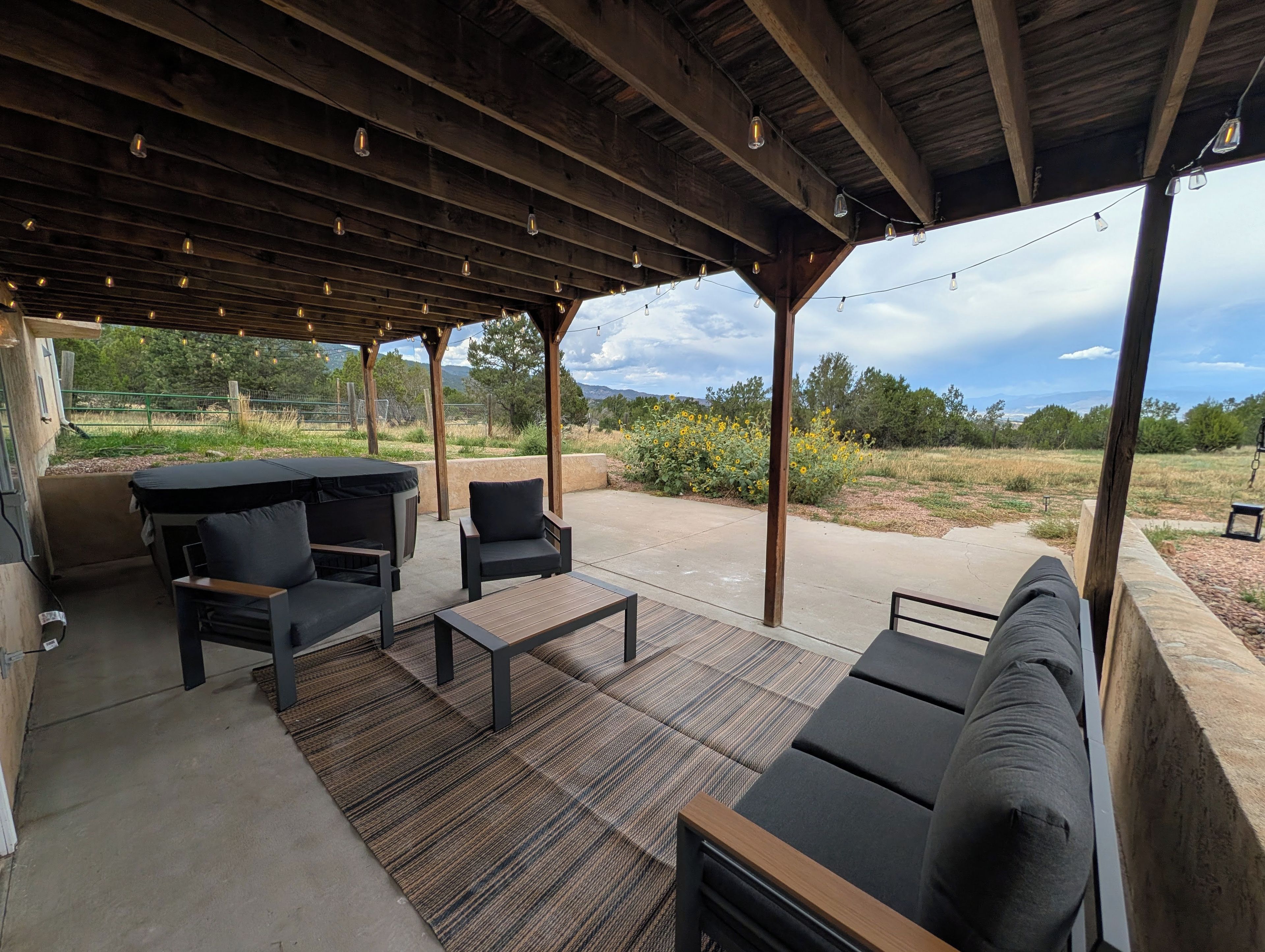 An outdoor patio with a wooden pergola, seating area, and a view of the surrounding landscape.