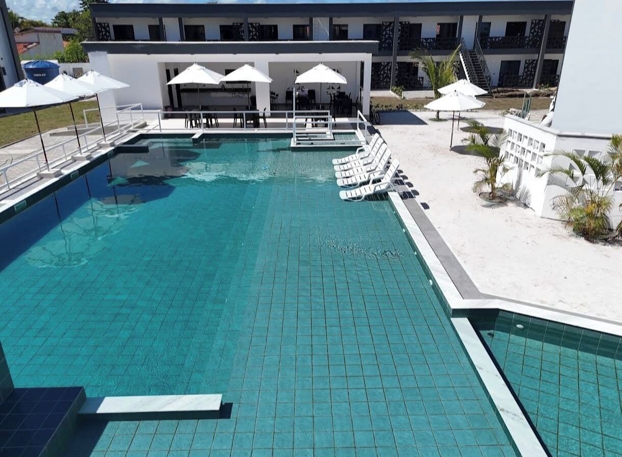 Ein Schwimmbecken mit Liegestühlen und Sonnenschirmen, ein überdachter Sitzbereich sowie ein Gebäude im Hintergrund.