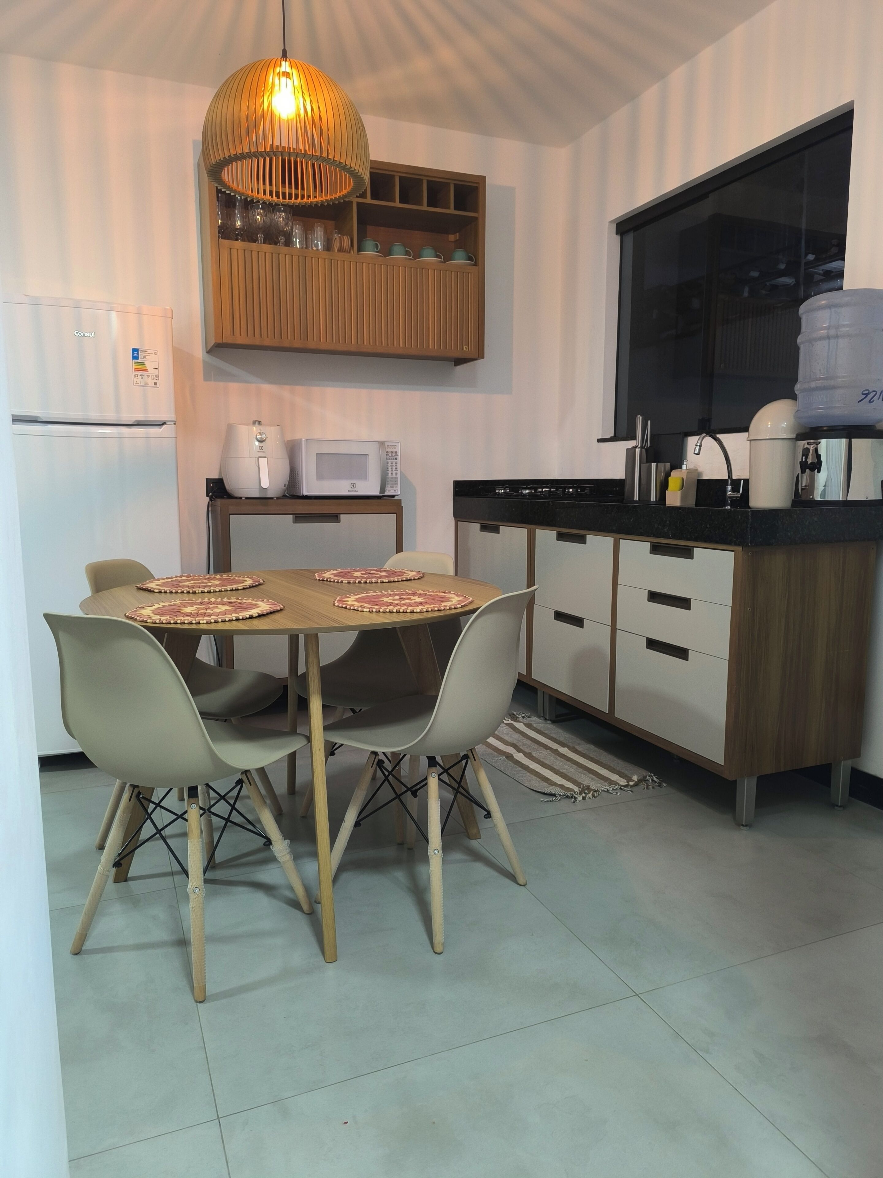 Eine moderne Küche mit Esstisch, Stühlen, einer Hängeleuchte, einer Mikrowelle und einem Kühlschrank.