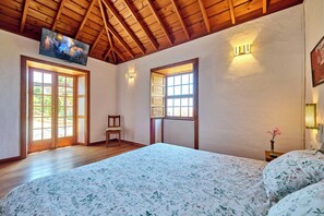Un dormitorio con una cama grande, vigas de madera en el techo y dos ventanas con cortinas.