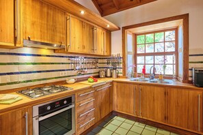 Una cocina con armarios de madera, estufa a gas, horno y una ventana con vista a zonas verdes, además de un respuesto de azulejos.