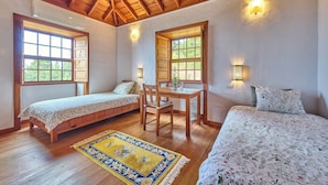 Una habitació amb dos llits, una taula de fusta i dues finestres amb lluminàries.