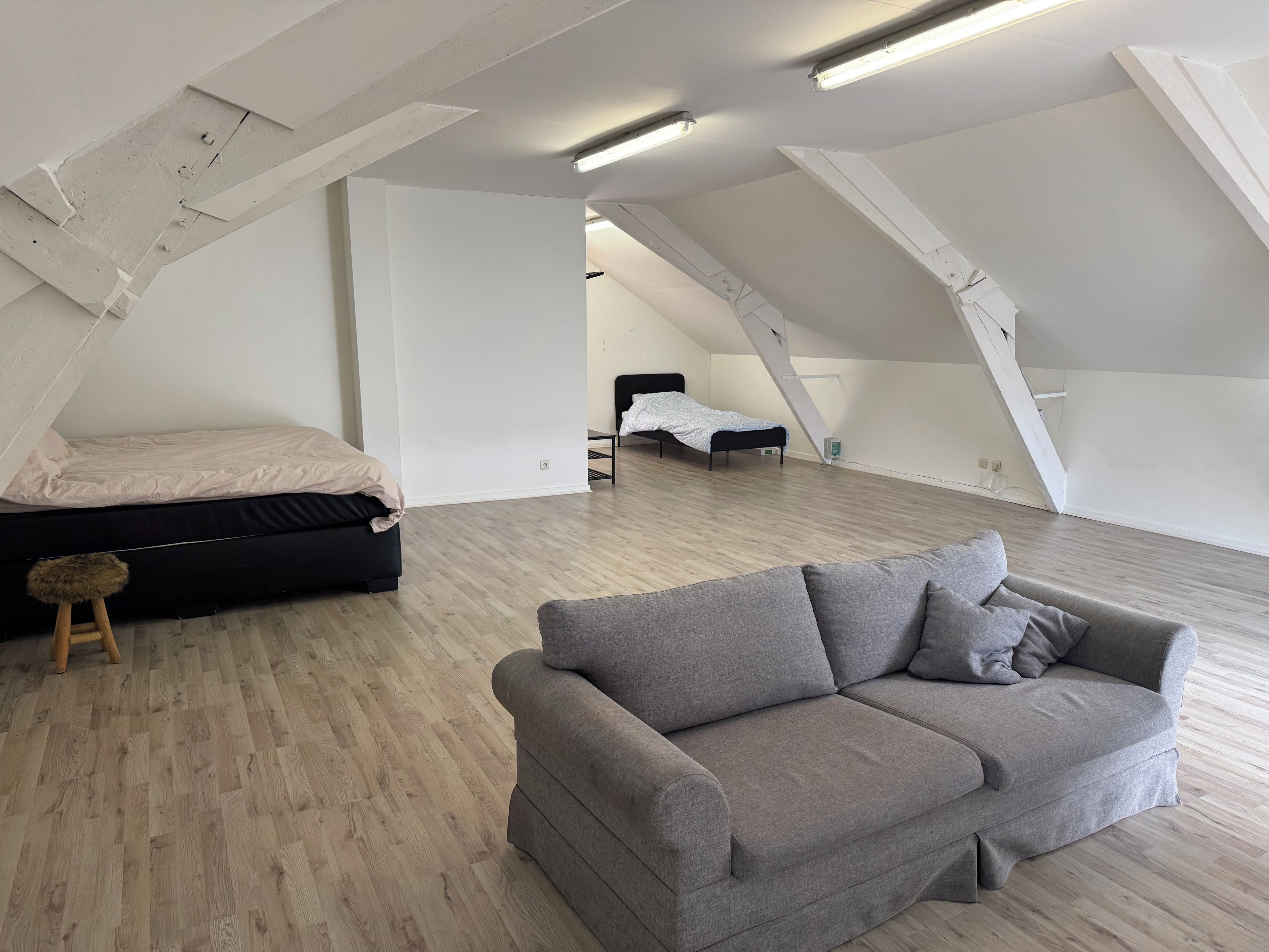 A spacious loft bedroom with a large gray sofa, a bed with a white cover, and a wooden floor.