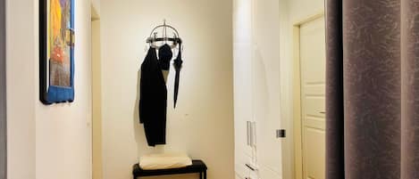 A hallway with a bench, a coat rack with a black coat and an umbrella, and a wardrobe with drawers.