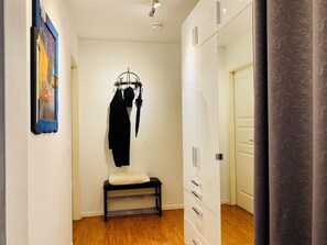 A hallway with a bench, a coat rack with a black coat and an umbrella, and a wardrobe with drawers. - Central 1 BR Apartment on Alexanderplatz (Berlin)