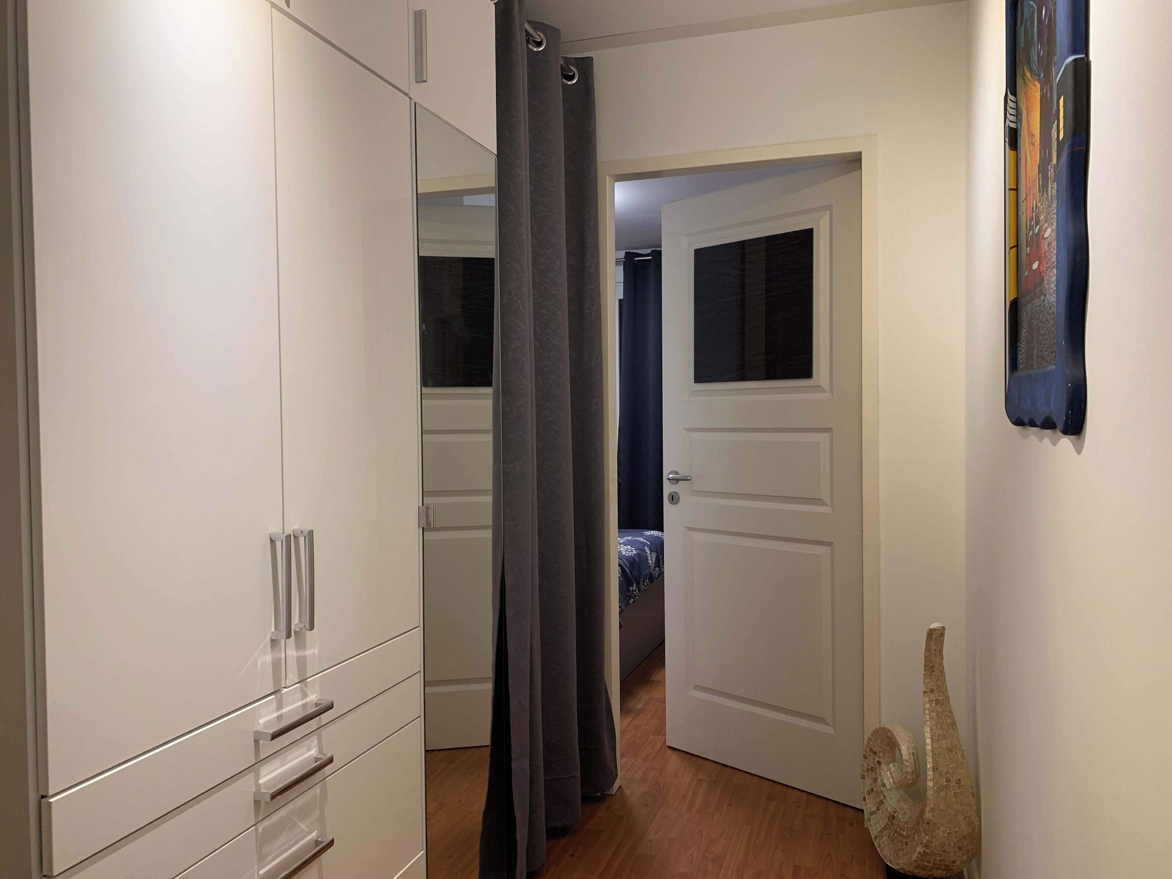 Ein Flur mit einem Schrank, einer zur Schlafzimmertür führenden Öffnung und einem Wanddekor.