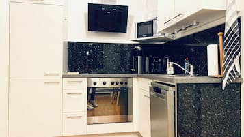 Eine kompakte Küche mit weißen Schränken, einem Edelstahlbackofen, einer Mikrowelle und einer Kaffeemaschine.