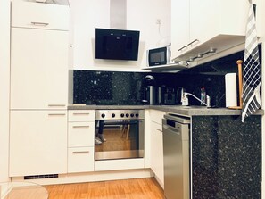 A compact kitchen with white cabinetry, a stainless steel oven, a microwave, and a coffee maker. - Central 1 BR Apartment on Alexanderplatz (Berlin)