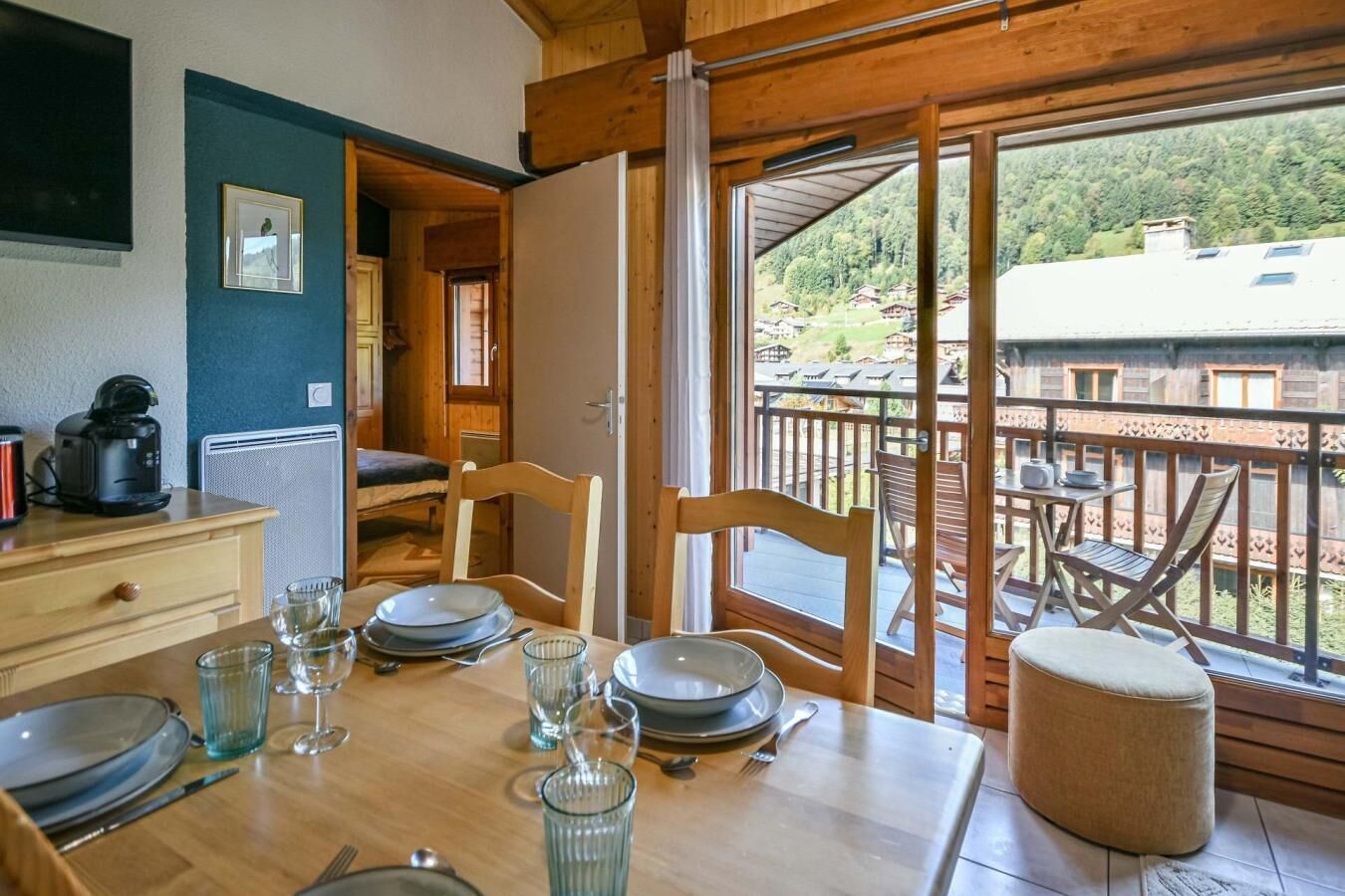 Un coin repas avec une table dressée pour quatre personnes, une machine à café et une vue sur un balcon aménagé avec du mobilier d’extérieur.