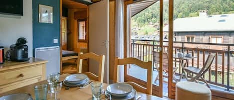 A dining area with a table set for four, a coffee maker, and a view of a balcony with outdoor furniture.