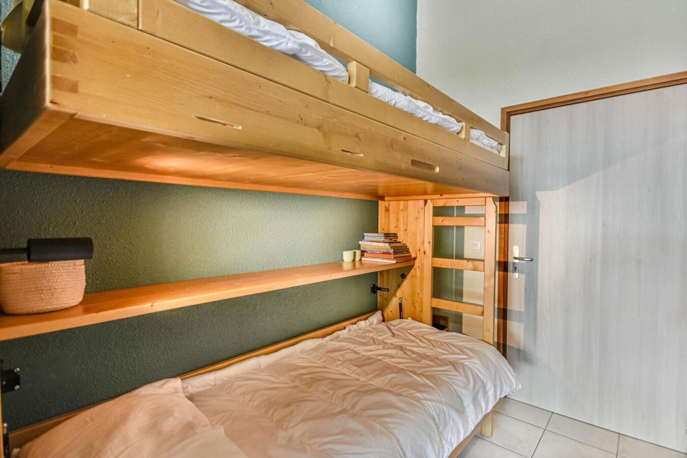 Een slaapkamer met een stapelbed, een groene muur, houten planken en een deur.