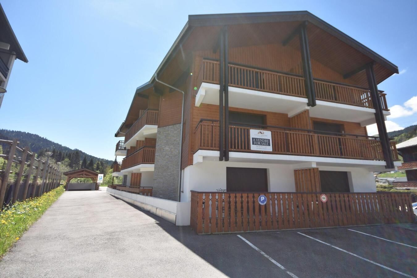 Un immeuble à plusieurs étages doté de balcons, d’un espace de stationnement et d’une enseigne indiquant qu’un bien est à vendre.