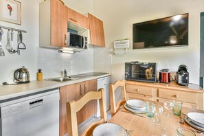 A compact kitchen with a microwave, oven, and coffee maker. There is a dishwasher and a dining table set with plates and glasses. - 300m from ski slopes, 2nd floor, balcony, parking, tv, ski locker, 35m², Les Gets (Les Gets)