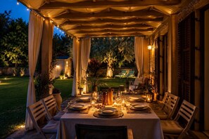 Un espace extérieur aménagé pour les repas, avec une table couverte pour quatre personnes, entourée de chaises, et offrant une vue sur un jardin et une maison en arrière-plan.