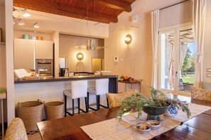 Une cuisine moderne dotée d’un îlot central, de tabourets de bar et d’une table à manger agrémentée d’un vase de plantes vertes.