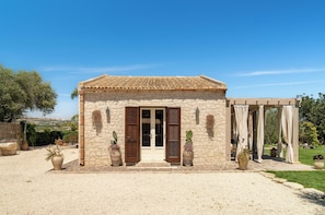 A stone building with a tiled roof, a wooden door, and a covered outdoor seating area. - Villa Ulìa SicilyMyHome (Ispica)