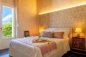 Une chambre d’hôtel avec un mur en pierre, un lit avec des oreillers, une table de chevet avec une lampe et une fenêtre avec des rideaux.