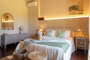 Une chambre avec un mur en pierre, un lit agrémenté d’oreillers à motifs, une table de chevet avec une lampe et une commode avec un miroir.