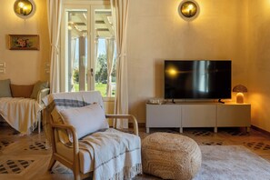Una sala acogedora con un sofá, un reposapiés y un televisor sobre un mueble blanco.