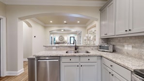 A modern kitchen with white cabinetry, granite countertops, stainless steel appliances, and a central island with a sink.
